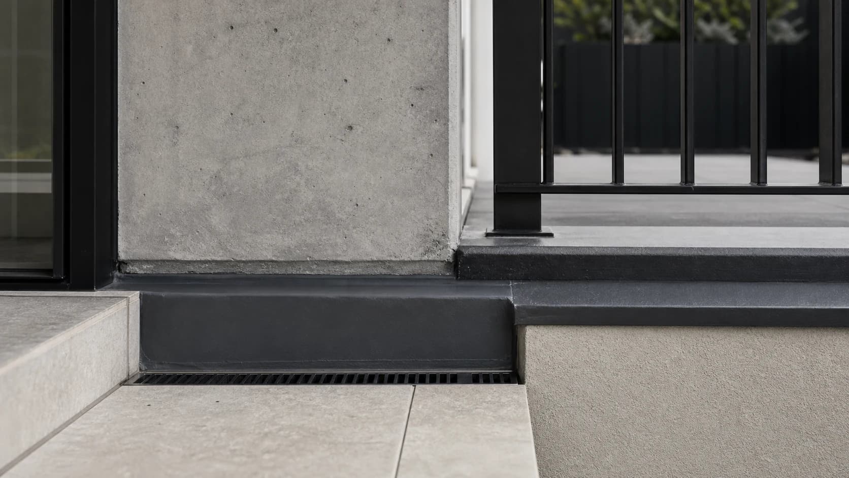 Architectural detail visual showing a concrete balcony edge, paving, drainage, and black metalwork