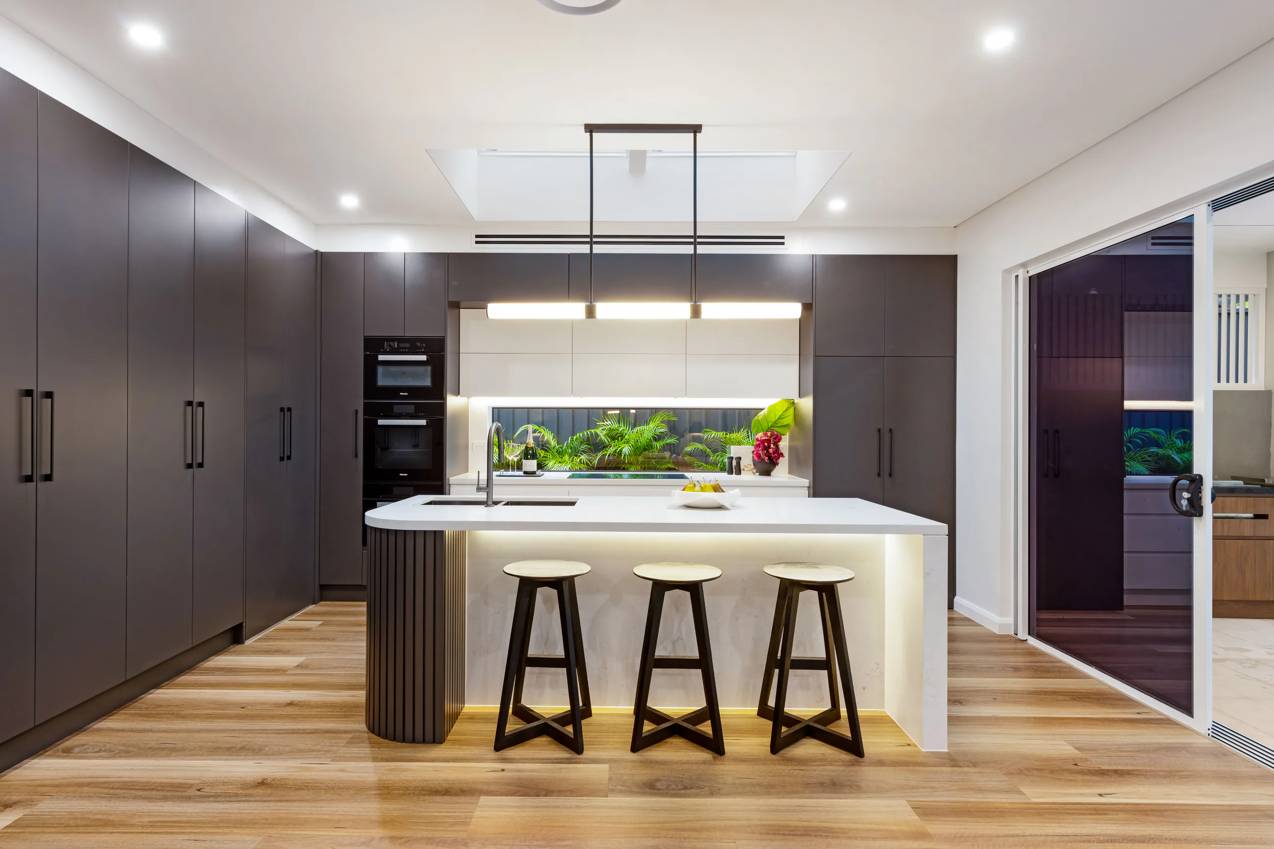 Cowell Renovation kitchen with dark full-height joinery, stone island, and warm timber flooring