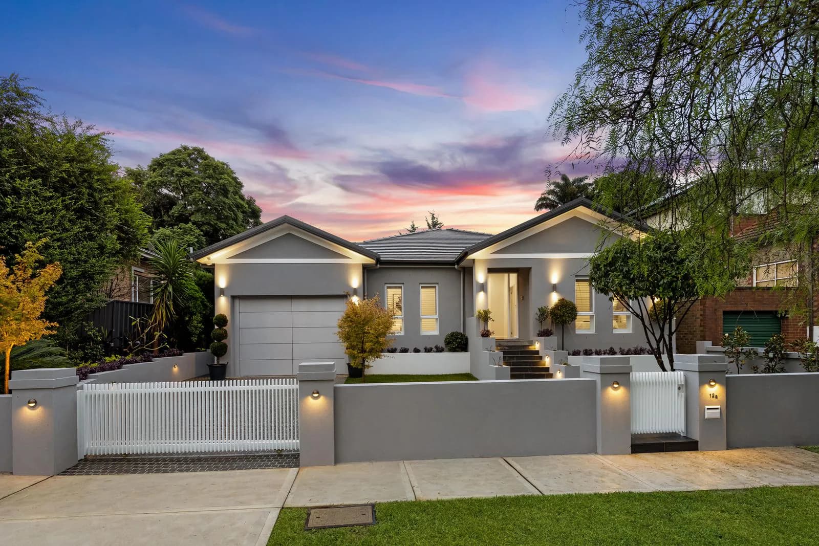Cowell Renovation street elevation at dusk with the original roof form, new landscaping, and illuminated entry