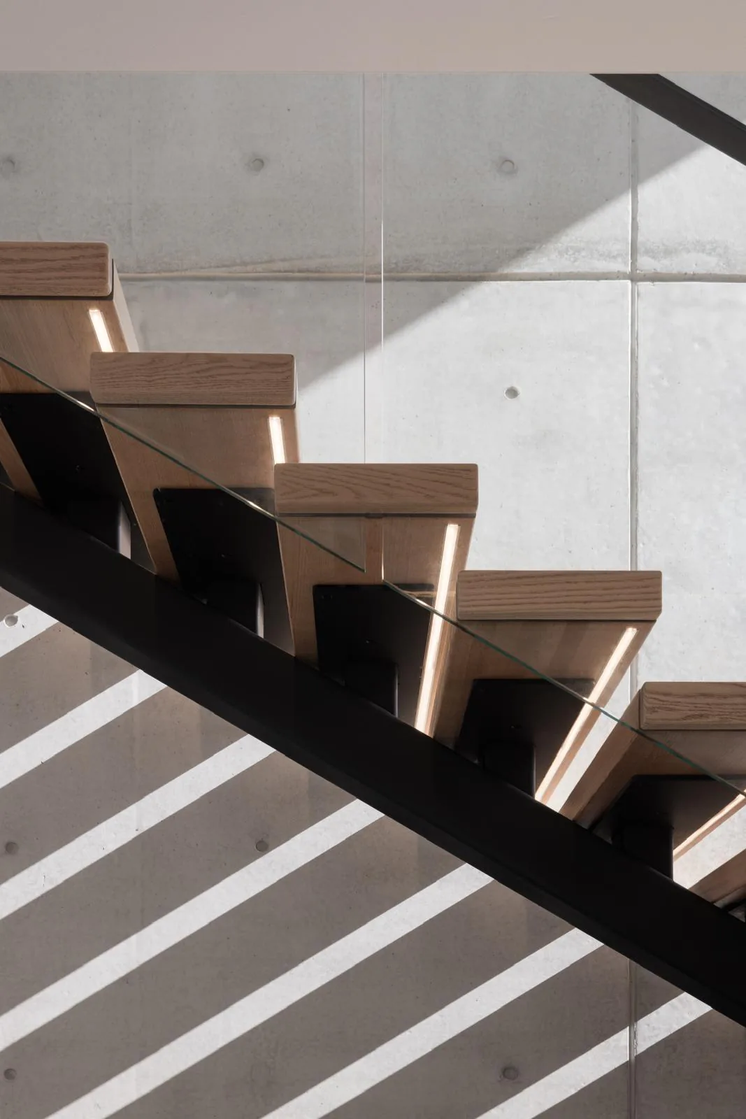 Open-riser timber staircase with black steel structure, glass balustrade, and concealed lighting