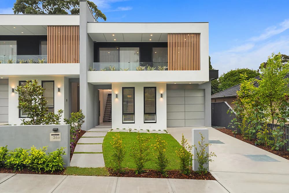 Front elevation of Paul Duplex with white concrete forms, timber screening, glass balconies, and landscaped entries