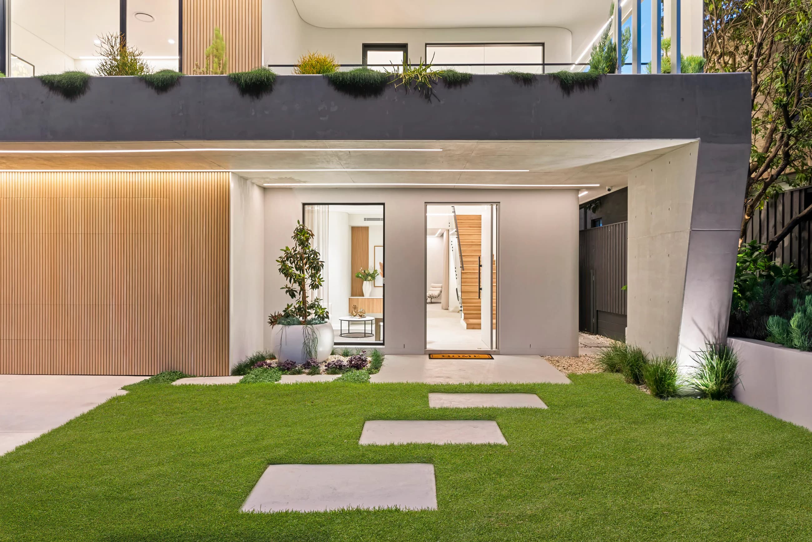 Landscaped front entry framed by curved concrete, timber battens, and dark glazing