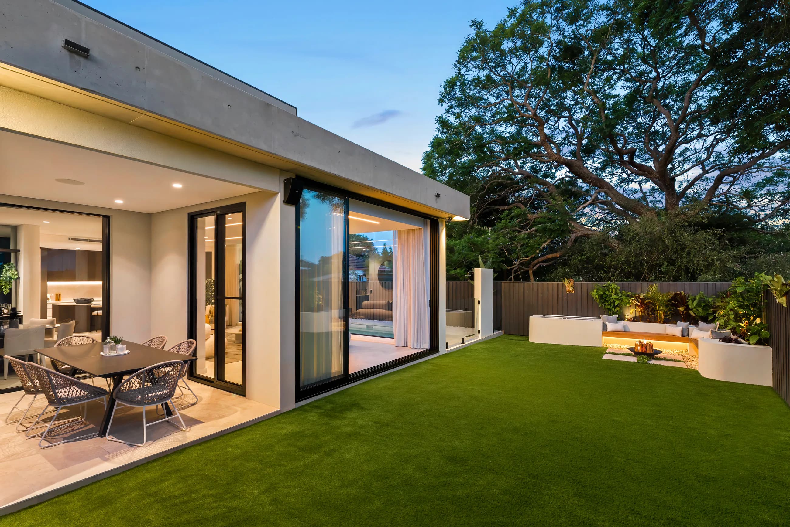 Ryrie Residence outdoor living area opening to a lawn and mature garden at dusk