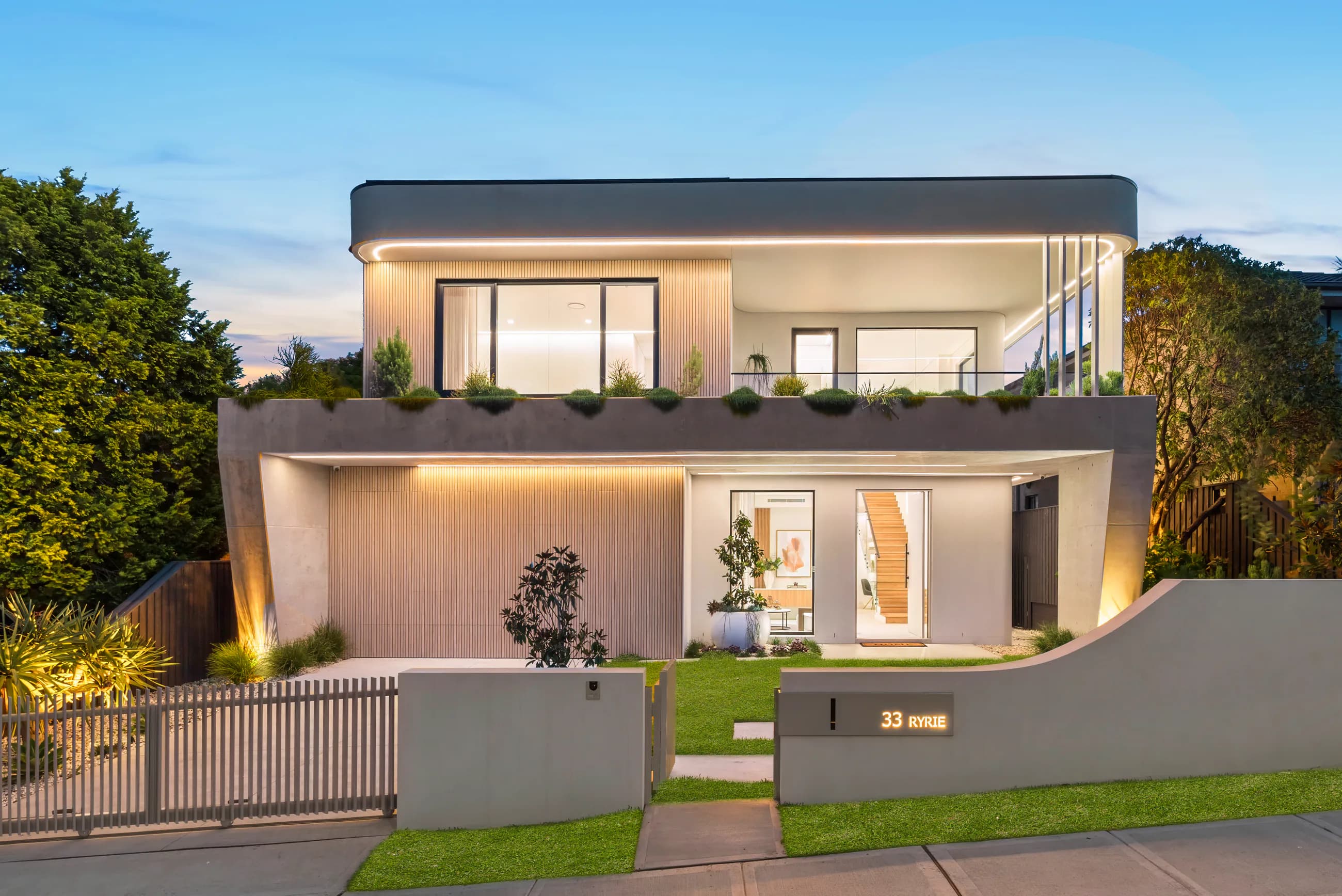 Ryrie Residence at dusk with curved white concrete forms, warm lighting, and layered landscaping